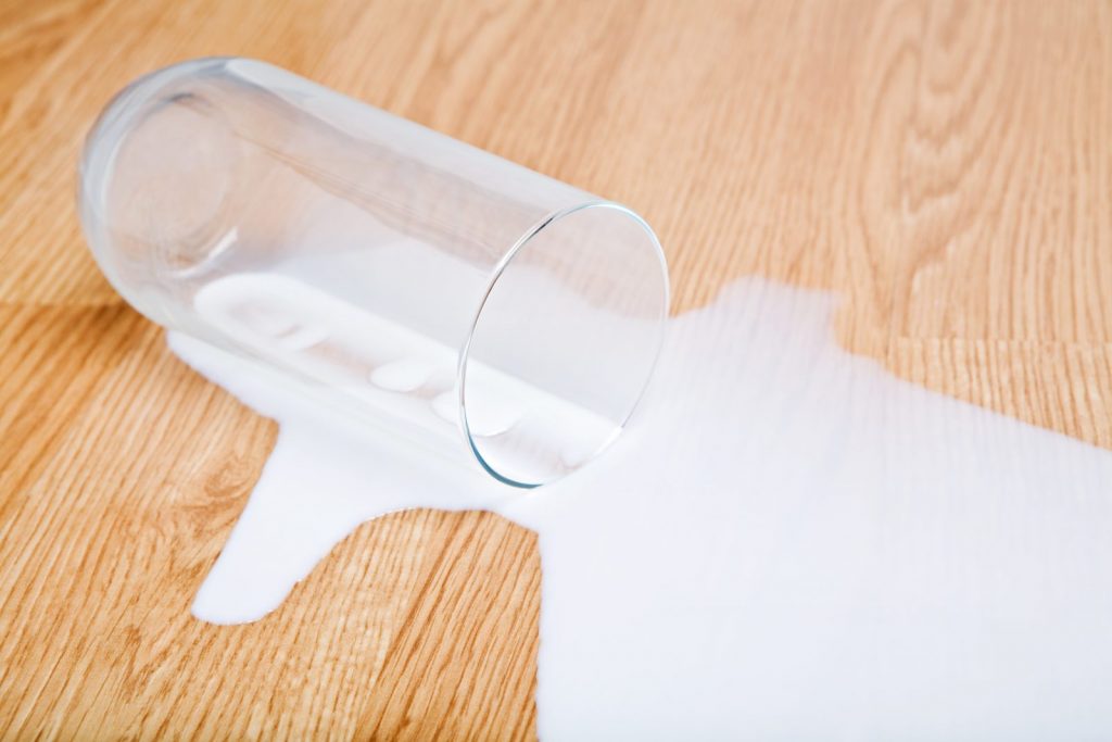 milk spilled from glass on oak wooden surface